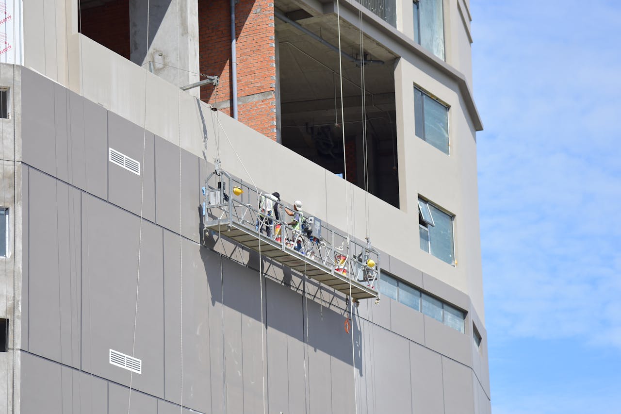 Construction workers on suspended scaffolding in an urban building exterior.