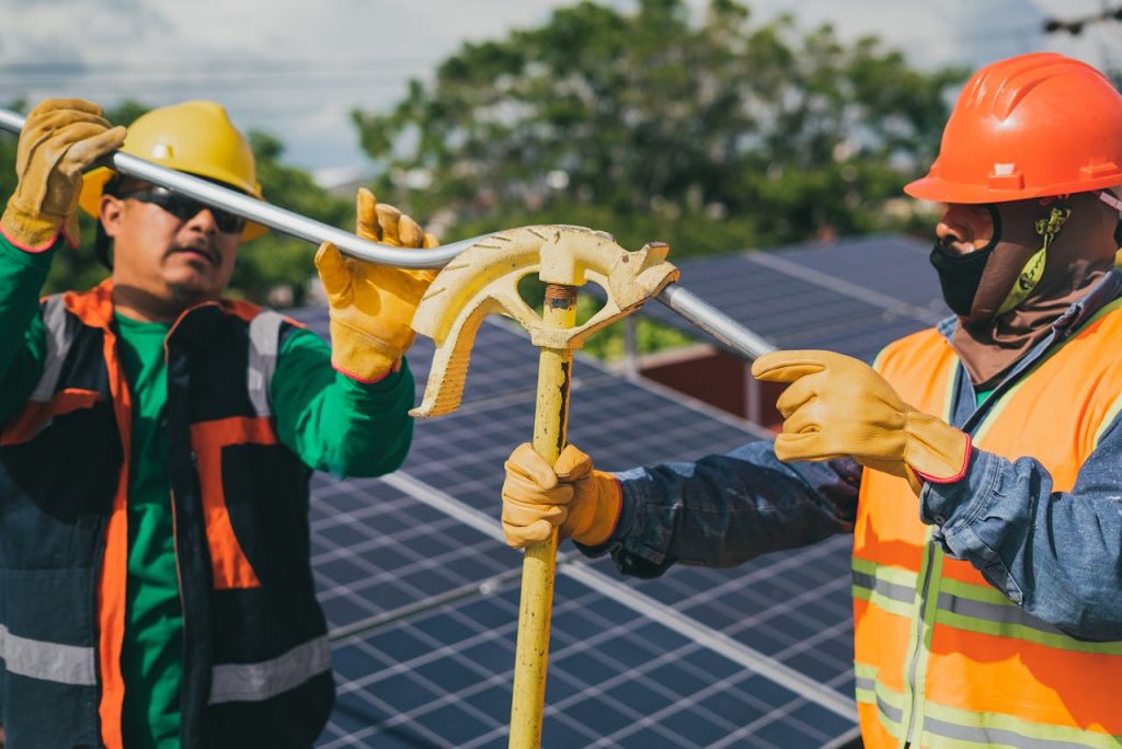 Two construction workers assembling solar panel equipment under sunny conditions, showcasing teamwork and renewable energy.