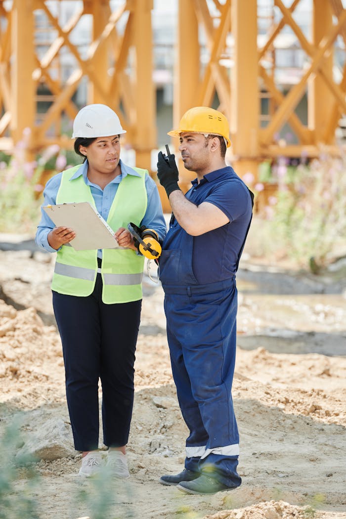 Two engineers in hard hats reviewing a construction plan at a building site.